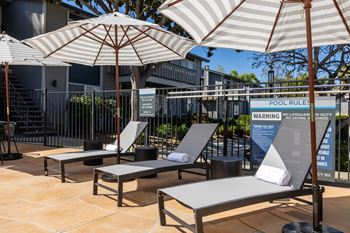 A group of lounge chairs with umbrellas in front of a building